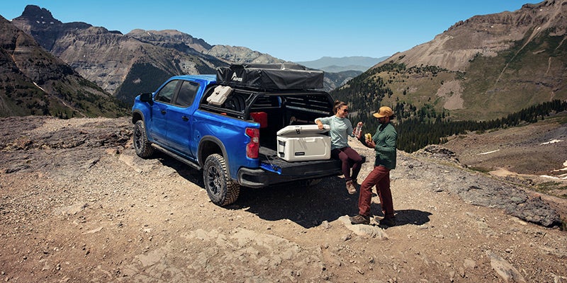Two people sitting on the tailgate of a blue truck.