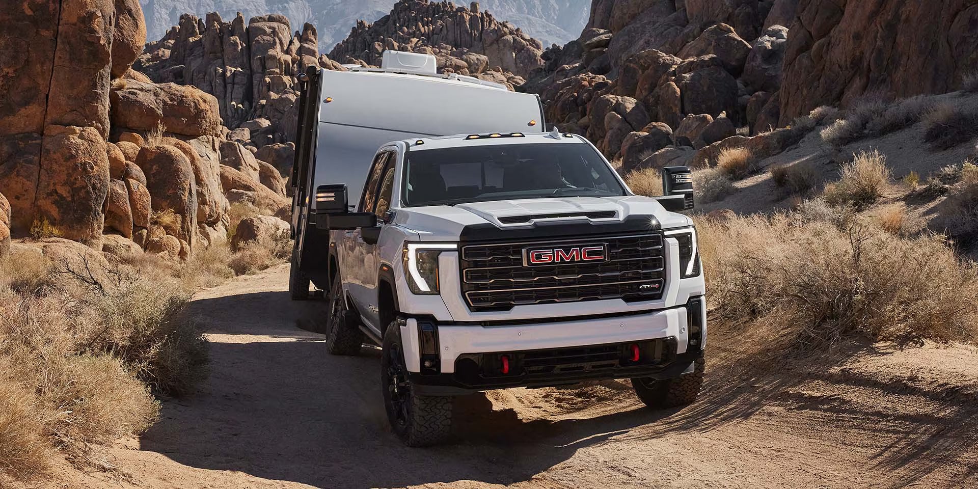 a white sierra hd hauling a camper in the desert