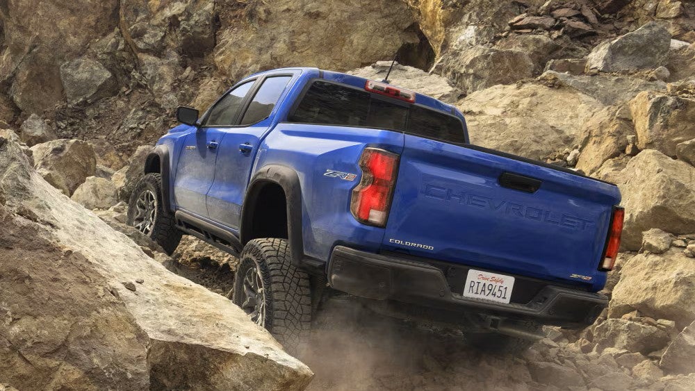 A blue truck driving up some rocks.