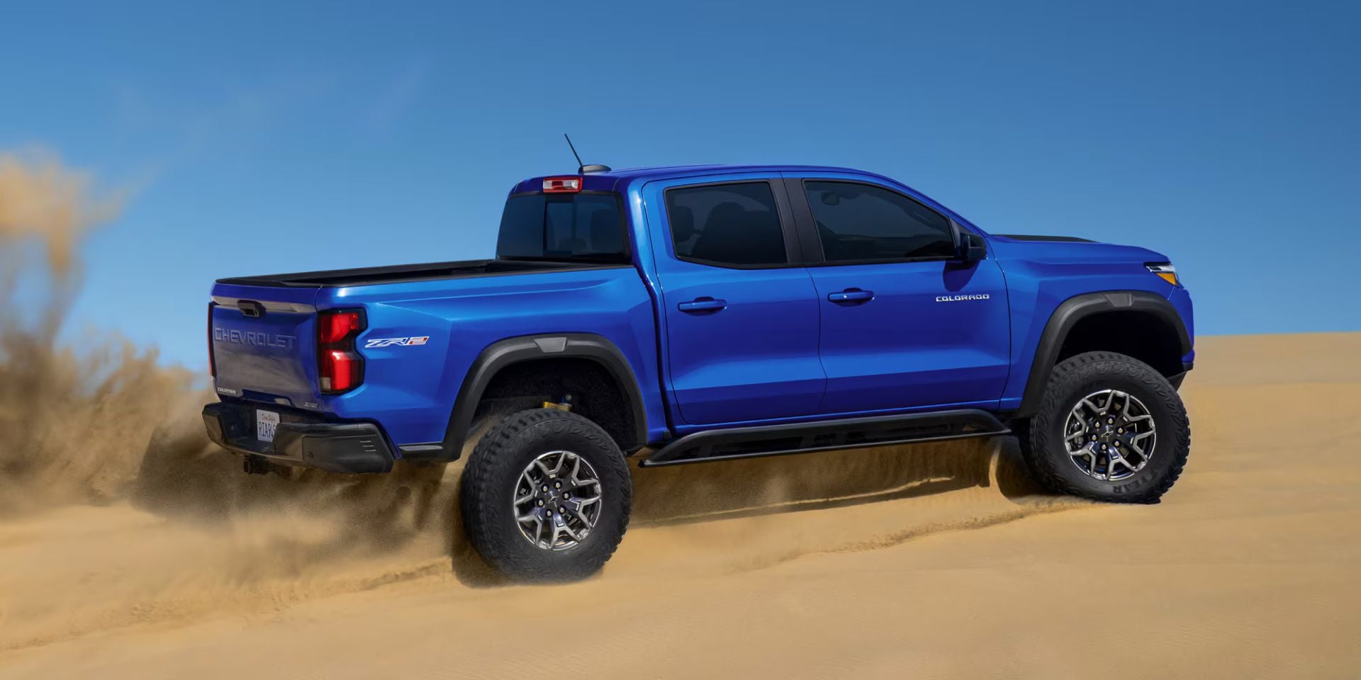 A blue truck driving through the sand.