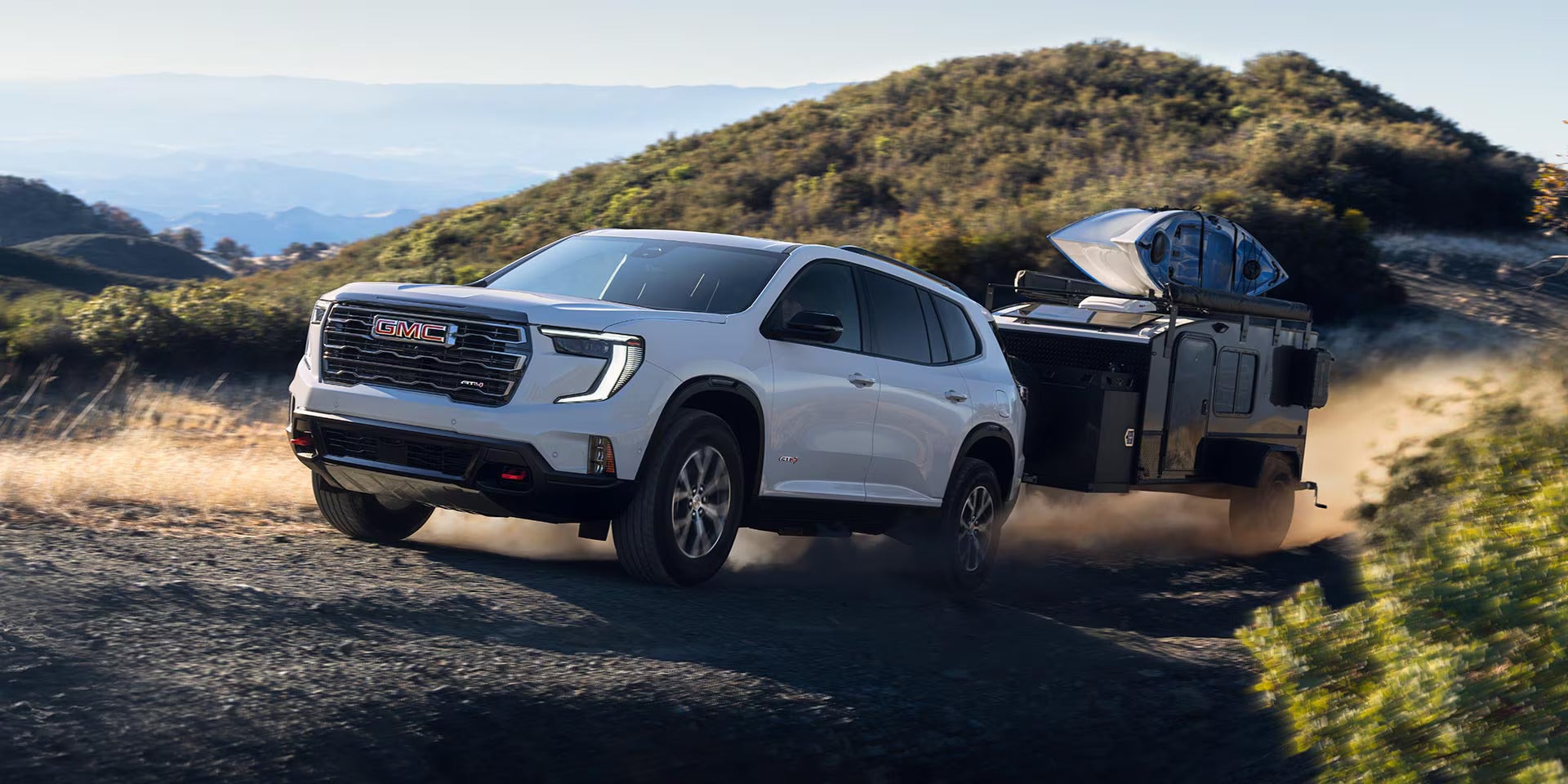 a white acadia driving donw a dirt path with a camper being hauled behind