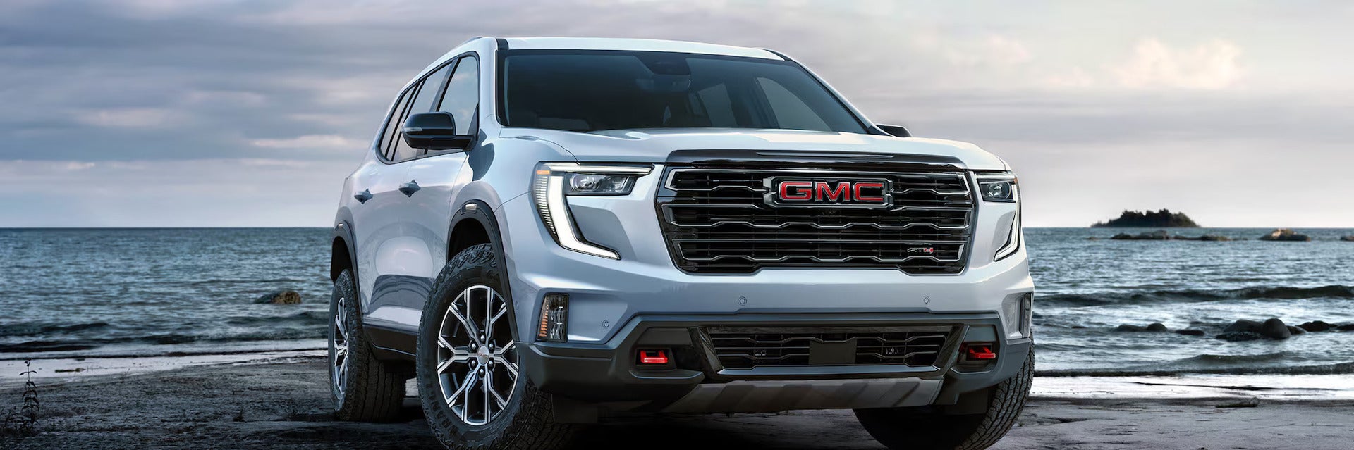 a white gmc acadia parked overlooking a cliff with the back open slightly and a woman walking towards it.