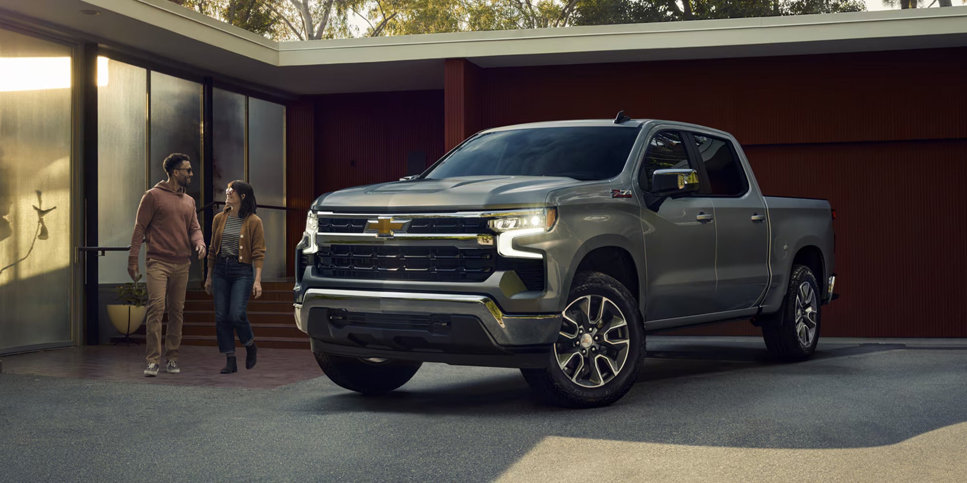 a man and woman standing next to a silverado 1500 parked at a house