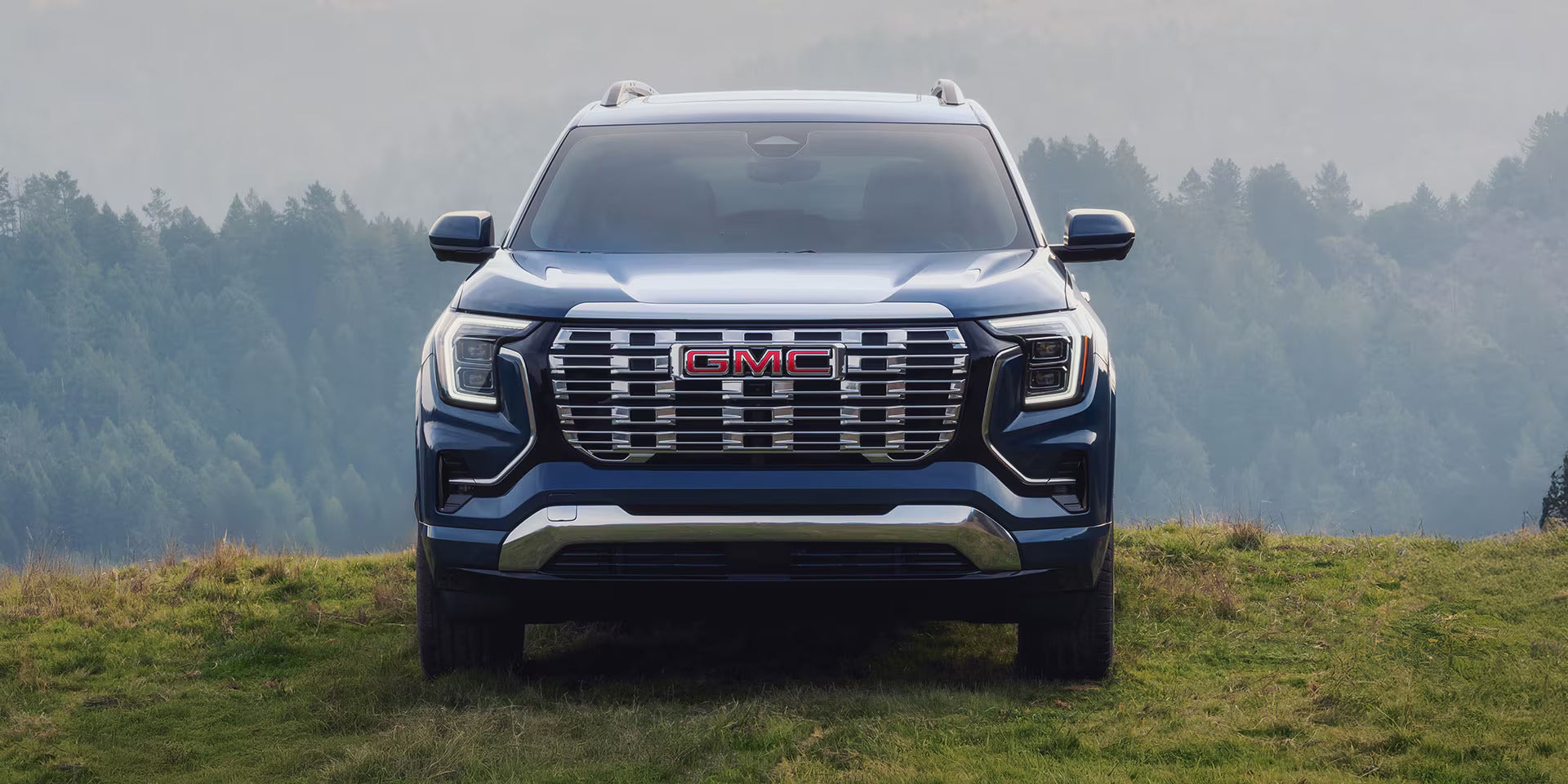 front view of the 2026 gmc terrain parked on grass overlooking mountains and trees