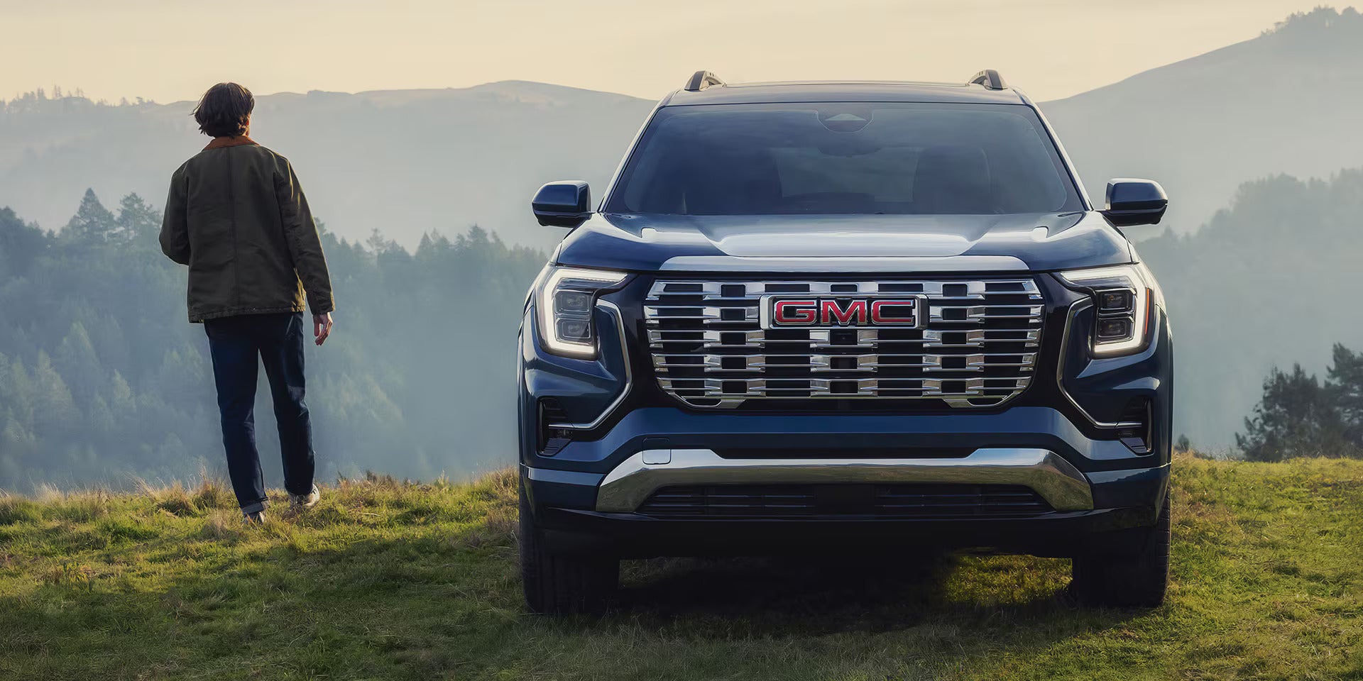 front view of a 2026 gmc terrain with a man looking at trees and mountains next to it.