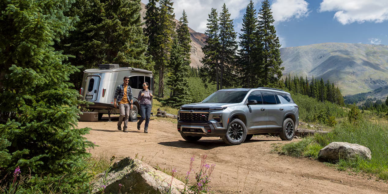 a chevy traverse parked next to a camper with people walking toward the traverse in the mountains